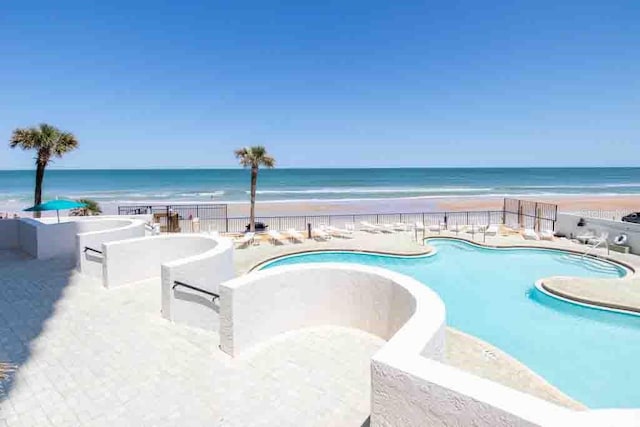 view of swimming pool with a water view, a view of the beach, and a patio area