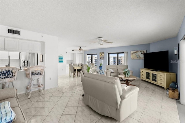 living room featuring a textured ceiling, light tile patterned floors, and ceiling fan