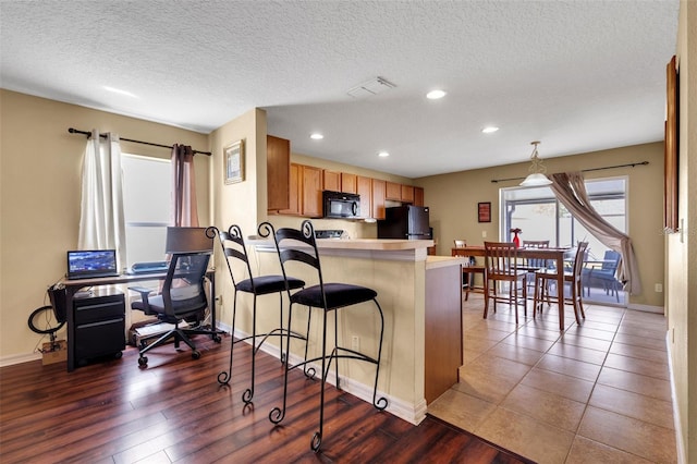 kitchen with hanging light fixtures, a textured ceiling, black appliances, kitchen peninsula, and hardwood / wood-style floors