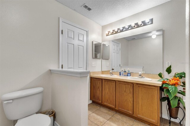 bathroom featuring vanity with extensive cabinet space, toilet, tile flooring, double sink, and a textured ceiling