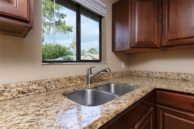 kitchen featuring sink, dark brown cabinetry, and light stone countertops