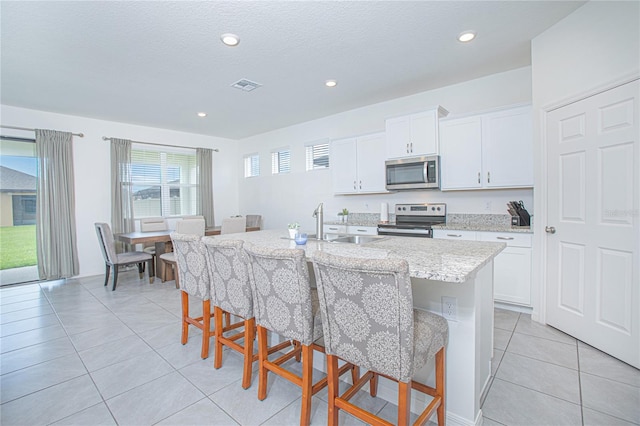 kitchen with appliances with stainless steel finishes, white cabinets, an island with sink, a breakfast bar area, and light tile patterned flooring