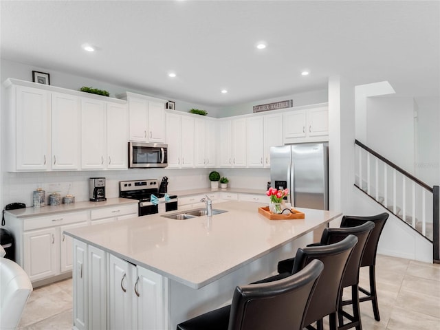 kitchen featuring a breakfast bar, a center island with sink, stainless steel appliances, light tile flooring, and white cabinetry