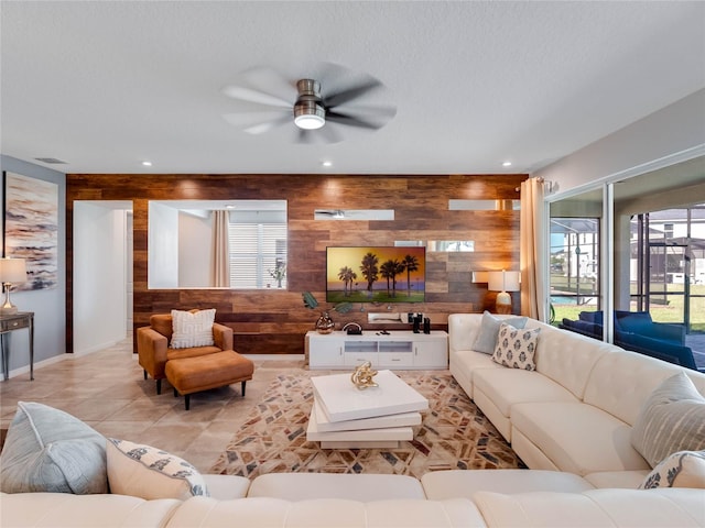 living room featuring wooden walls, a textured ceiling, ceiling fan, and light tile flooring