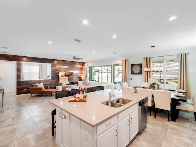 kitchen featuring wood walls, white cabinets, a kitchen island with sink, dishwasher, and sink