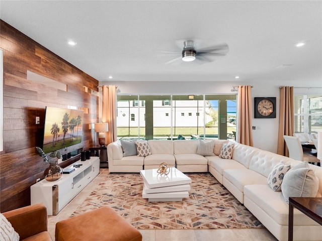 living room featuring wooden walls, ceiling fan, and a healthy amount of sunlight