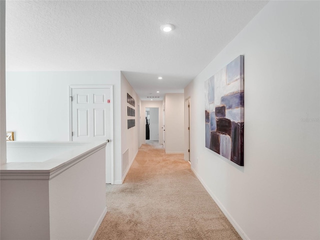 corridor with light carpet and a textured ceiling