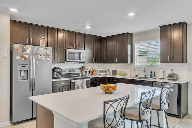 kitchen with appliances with stainless steel finishes, a kitchen island, a kitchen bar, sink, and light tile flooring