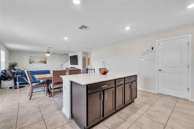 kitchen with ceiling fan, a kitchen island, dark brown cabinetry, and light tile floors