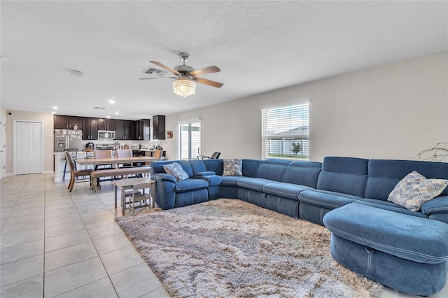 living room with a textured ceiling, ceiling fan, and light tile floors