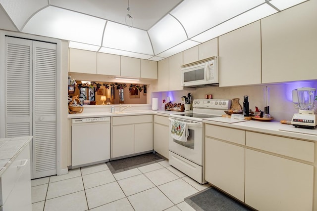 kitchen featuring white appliances, sink, cream cabinets, and light tile floors