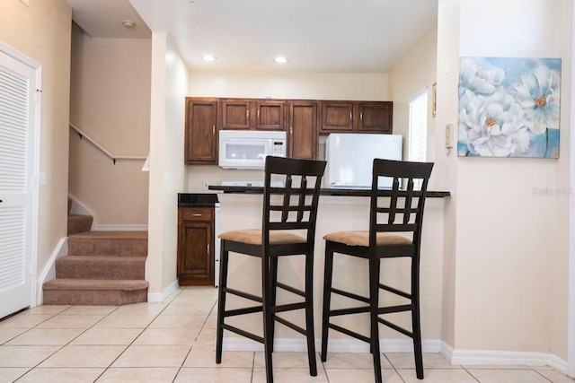 kitchen featuring light tile patterned flooring, white appliances, and a kitchen breakfast bar