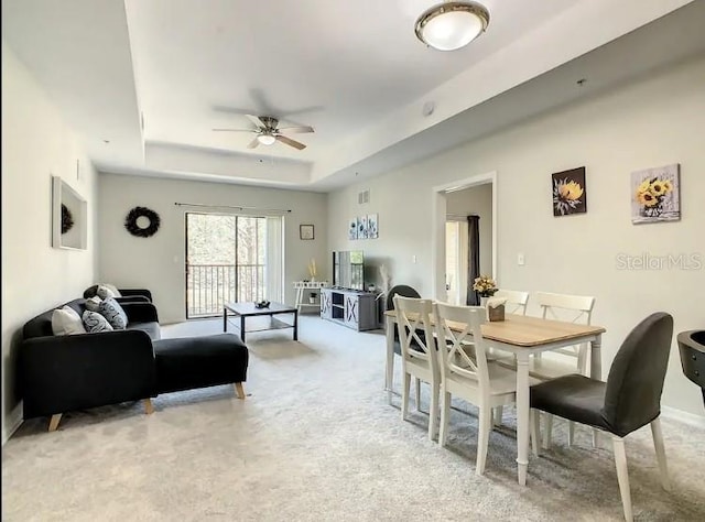 dining room featuring a raised ceiling, ceiling fan, and light colored carpet