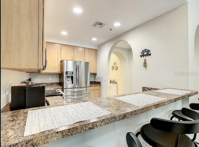 kitchen with light brown cabinetry, a breakfast bar area, and stainless steel fridge