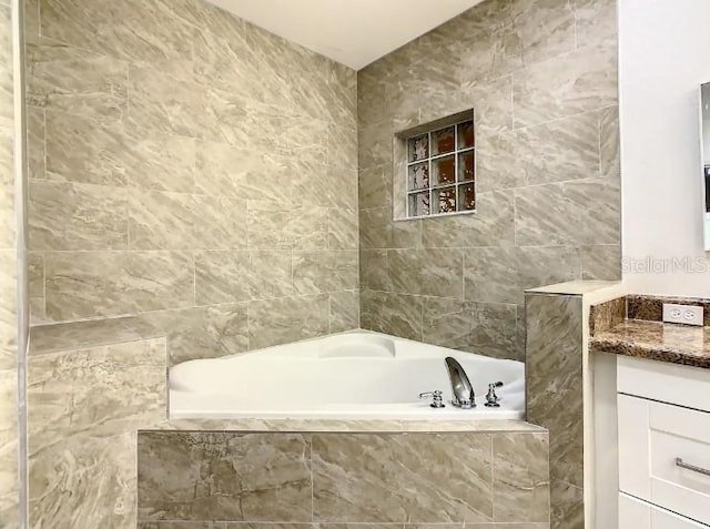 bathroom with tile walls, a relaxing tiled bath, and vanity