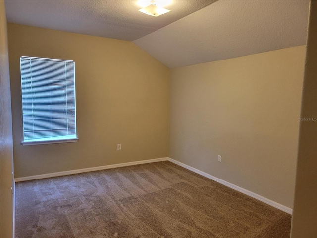 spare room with a textured ceiling, dark carpet, and lofted ceiling