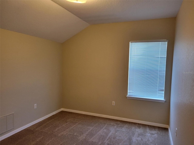 spare room with a textured ceiling, dark colored carpet, and vaulted ceiling