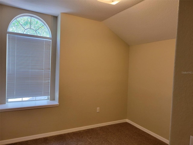 empty room featuring a textured ceiling, vaulted ceiling, and dark colored carpet