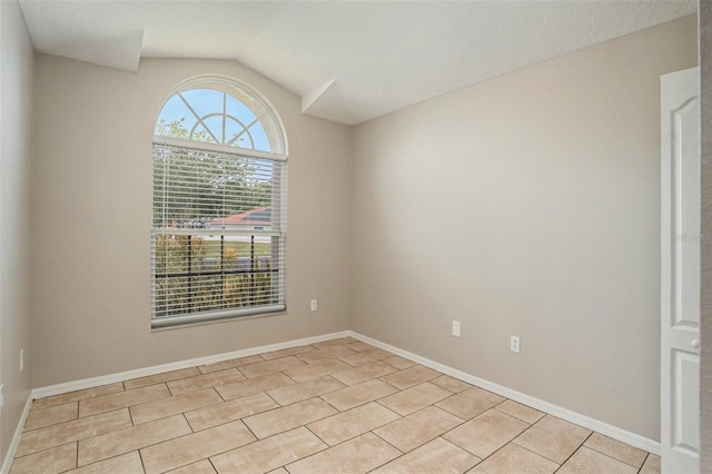 spare room featuring a healthy amount of sunlight, light tile floors, and lofted ceiling