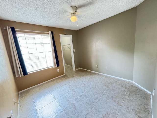 unfurnished bedroom with light tile patterned flooring, a closet, ceiling fan, a walk in closet, and a textured ceiling