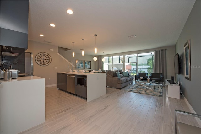 kitchen with an island with sink, pendant lighting, stainless steel appliances, light hardwood / wood-style flooring, and sink