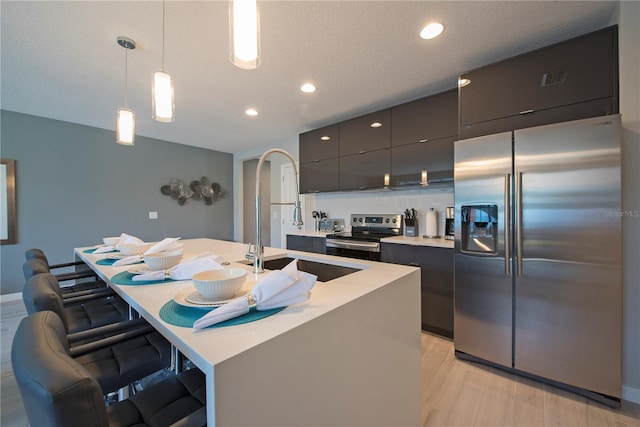 kitchen featuring decorative light fixtures, a kitchen bar, appliances with stainless steel finishes, a kitchen island with sink, and light wood-type flooring