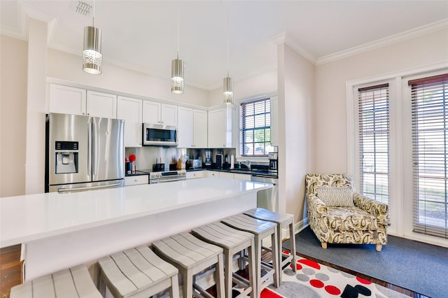 kitchen featuring stainless steel appliances, ornamental molding, pendant lighting, a kitchen island, and white cabinets