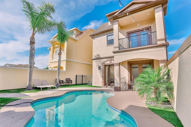 rear view of house with a balcony, a patio, french doors, and a fenced in pool