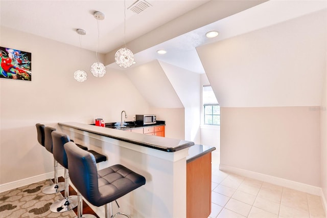 kitchen featuring kitchen peninsula, a breakfast bar, pendant lighting, sink, and light tile patterned flooring