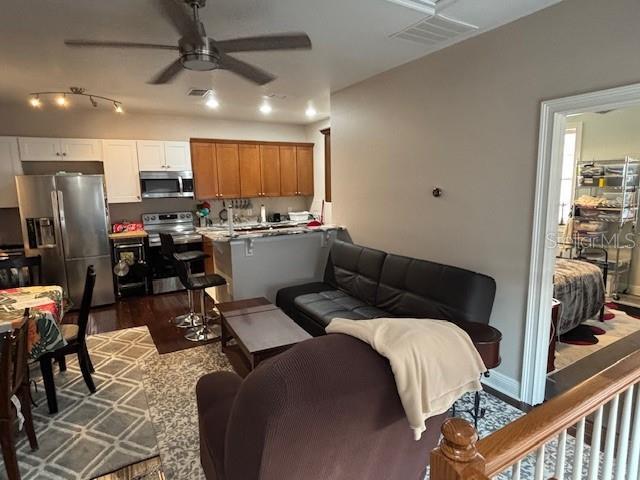 living area featuring dark wood-type flooring, visible vents, and a ceiling fan