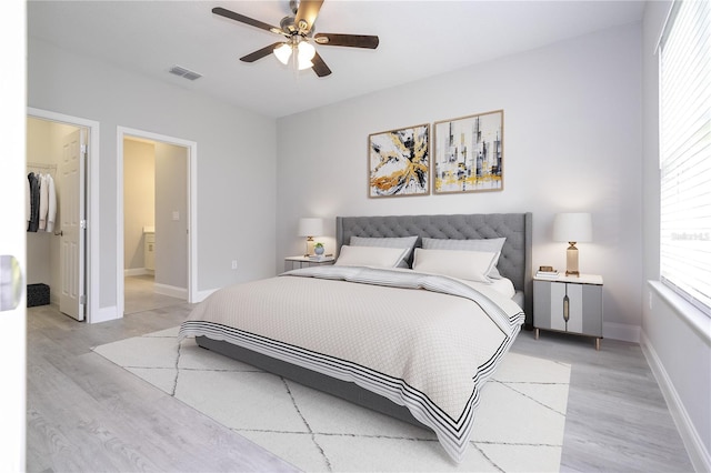 bedroom featuring light wood-type flooring, a closet, a spacious closet, ensuite bathroom, and ceiling fan