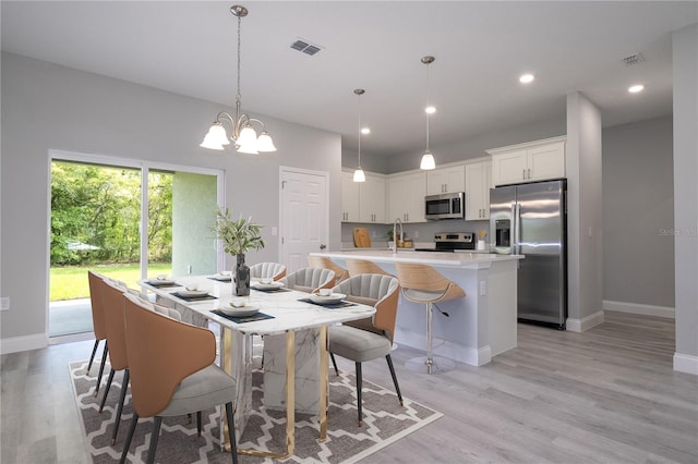 kitchen featuring appliances with stainless steel finishes, decorative light fixtures, light wood-type flooring, a kitchen island with sink, and white cabinets