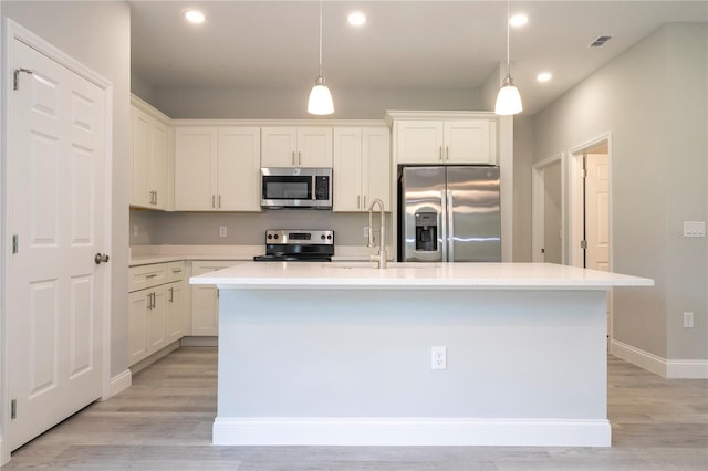 kitchen with appliances with stainless steel finishes, a kitchen island with sink, light hardwood / wood-style floors, and hanging light fixtures