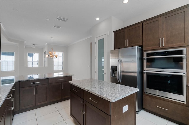 kitchen featuring a chandelier, stainless steel appliances, a center island, hanging light fixtures, and light stone counters