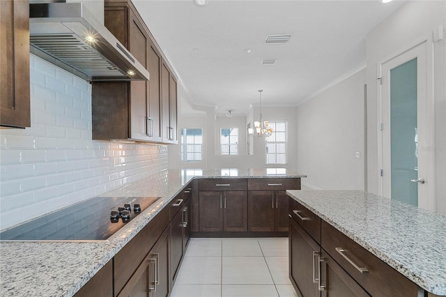 kitchen featuring backsplash, light stone countertops, wall chimney exhaust hood, a notable chandelier, and black electric stovetop