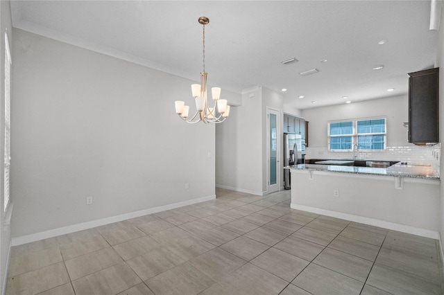 kitchen featuring an inviting chandelier, pendant lighting, light stone counters, backsplash, and ornamental molding