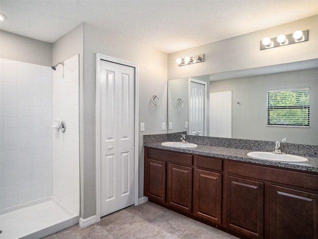 bathroom featuring a textured ceiling, dual bowl vanity, tile floors, and a tile shower