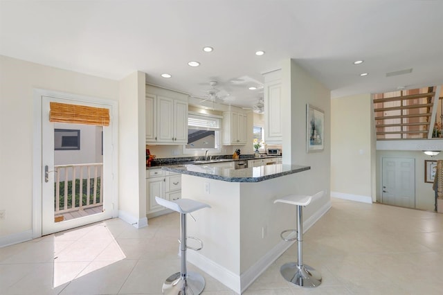 kitchen featuring ceiling fan, light tile floors, white cabinetry, dark stone countertops, and a kitchen breakfast bar