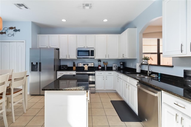 kitchen with stainless steel appliances, light tile floors, a center island, dark stone counters, and white cabinetry