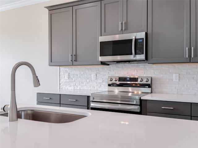 kitchen featuring sink, crown molding, gray cabinetry, backsplash, and stainless steel appliances