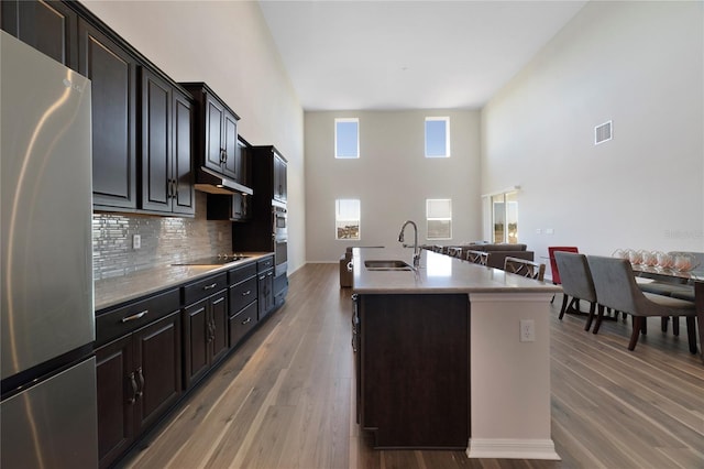 kitchen featuring sink, an island with sink, stainless steel refrigerator, hardwood / wood-style floors, and a high ceiling