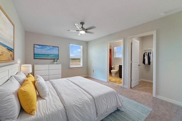 carpeted bedroom featuring ensuite bath, ceiling fan, a walk in closet, and a closet