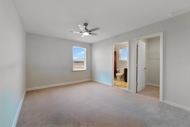 unfurnished bedroom featuring connected bathroom, a closet, ceiling fan, a walk in closet, and light carpet