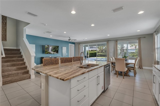 kitchen featuring stainless steel dishwasher, ceiling fan, white cabinetry, a kitchen island with sink, and sink