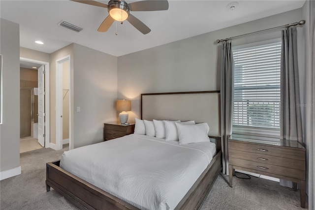 bedroom with ceiling fan, light colored carpet, and ensuite bathroom