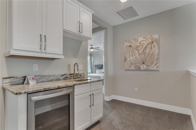 kitchen featuring dark colored carpet, ceiling fan, beverage cooler, sink, and white cabinets