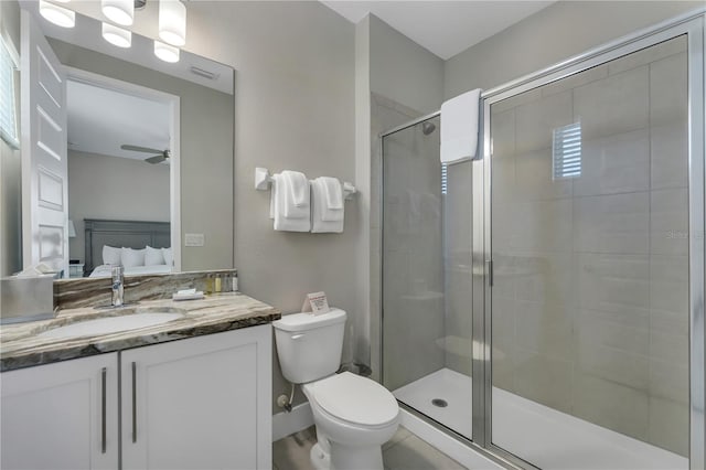 bathroom featuring a shower with shower door, toilet, vanity with extensive cabinet space, and ceiling fan