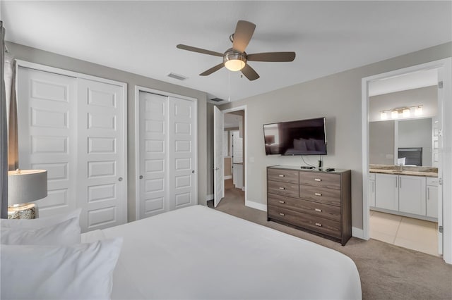 bedroom featuring multiple closets, ceiling fan, light carpet, and ensuite bathroom