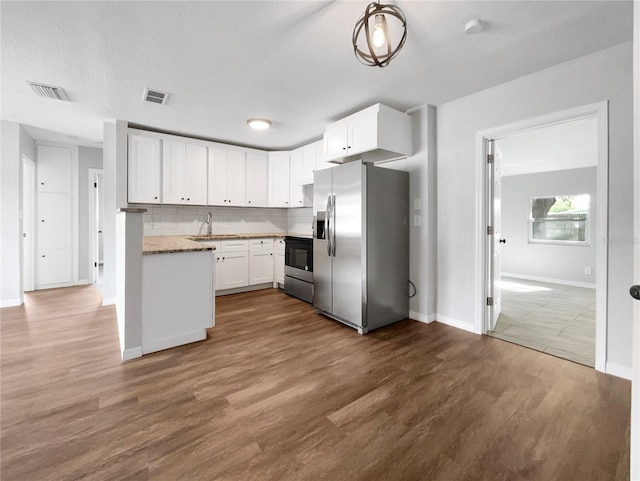 kitchen with stainless steel fridge, stove, white cabinets, light stone countertops, and tasteful backsplash