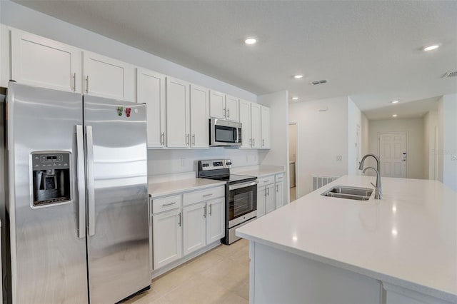 kitchen featuring an island with sink, stainless steel appliances, light tile floors, white cabinetry, and sink